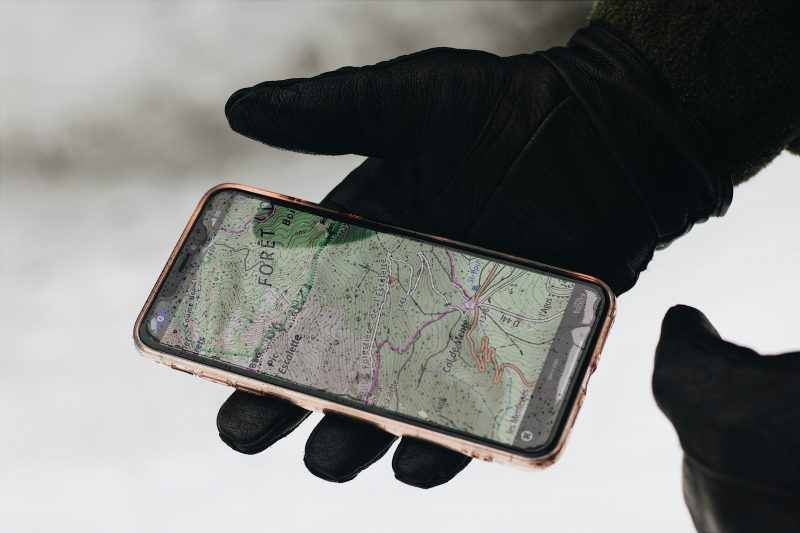 A gloved hand holds a smartphone with a map app displayed, showcasing navigation in cold weather.